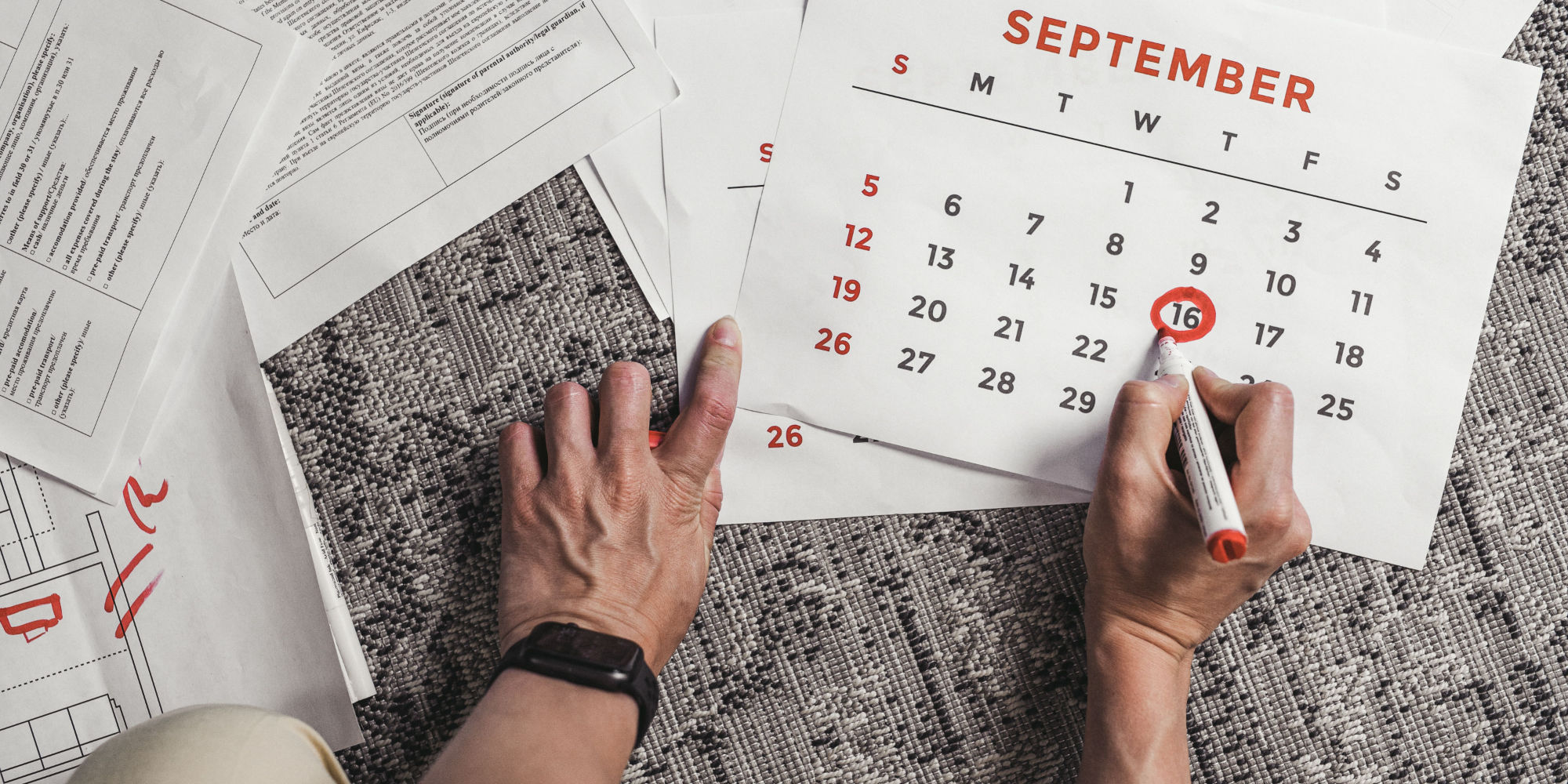 A hand circling a date on a paper calendar laid over stacks of corporate paperwork