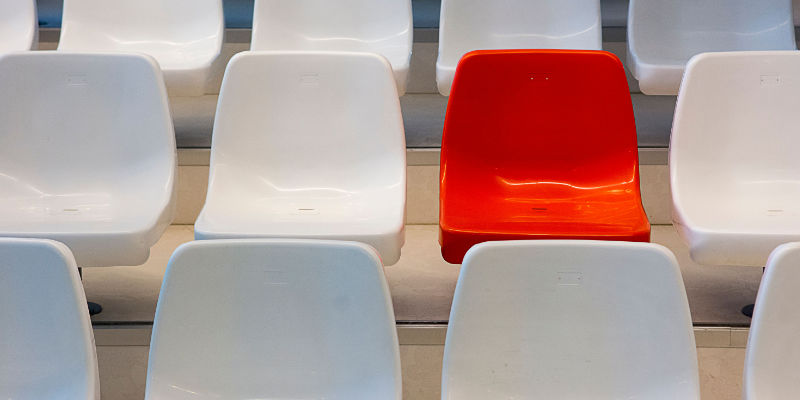 A single red seat standing out among rows of identical white seats