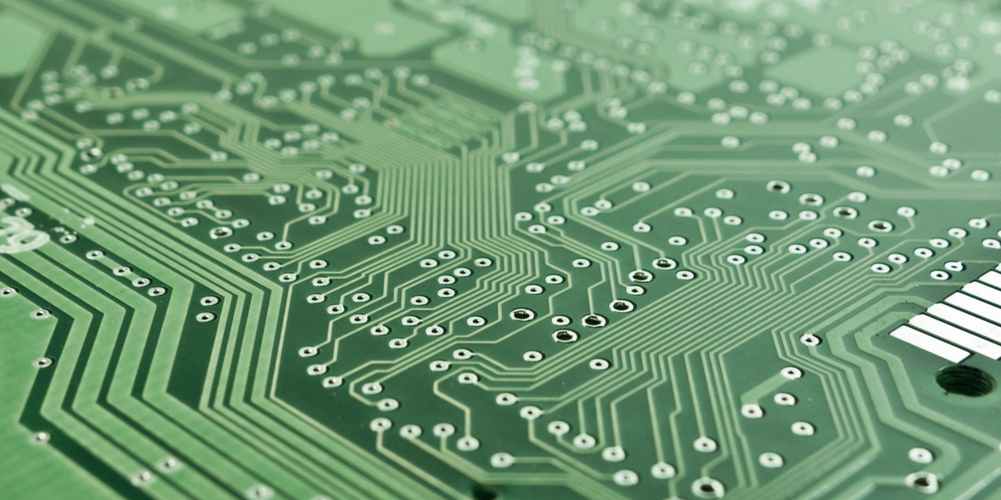 Close-up of a green printed circuit board showing copper traces and solder pads